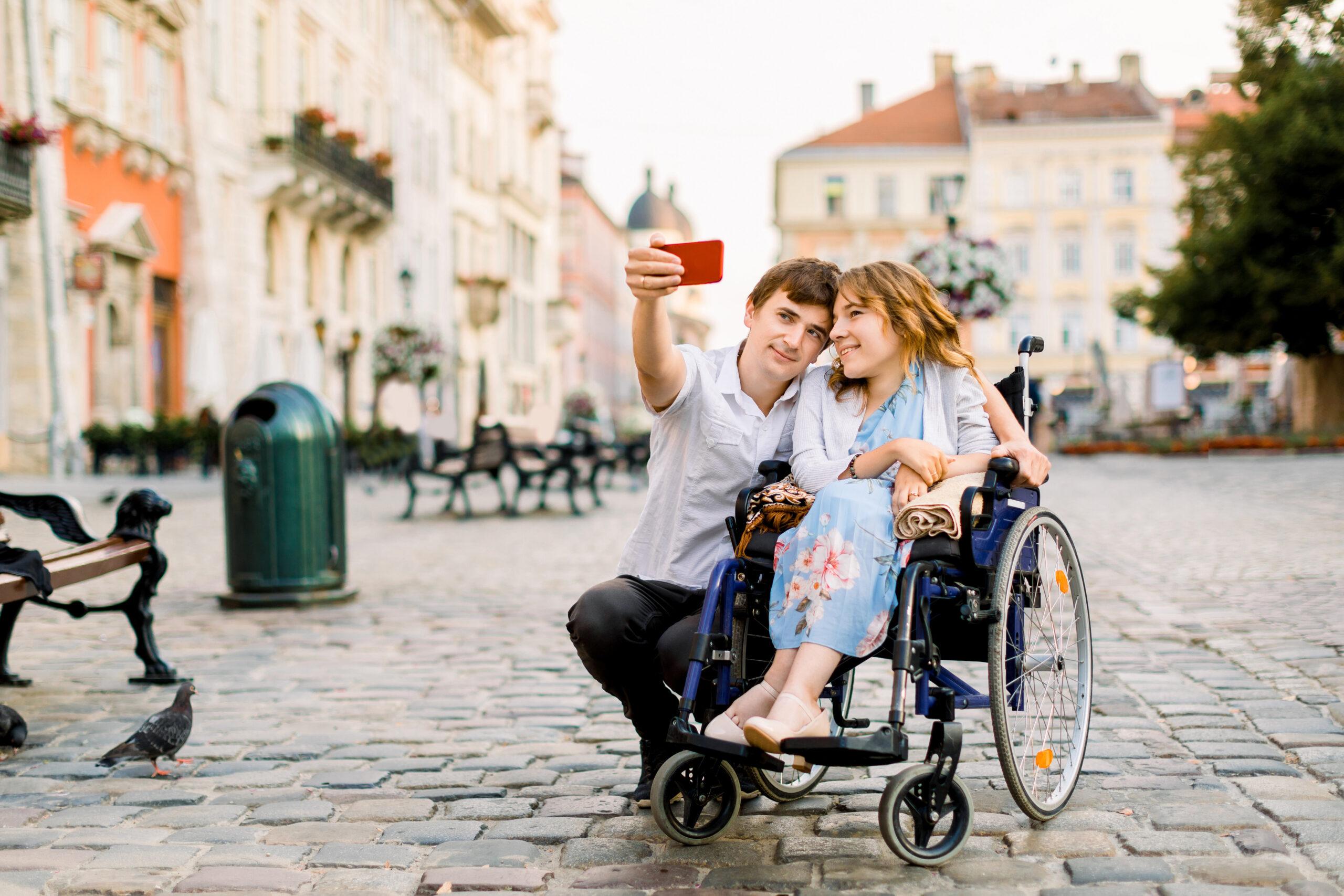 selfie time. handsome happy young man hugging his disabled young pretty woman and smiling while taking selfie with her in the city aide à la personne